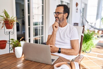 Fototapeta premium Middle age man using computer laptop at home with hand on chin thinking about question, pensive expression. smiling and thoughtful face. doubt concept.