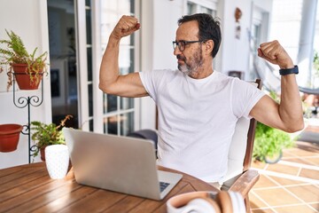 Middle age man using computer laptop at home showing arms muscles smiling proud. fitness concept.