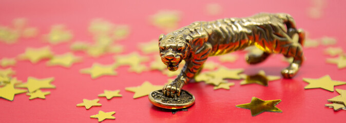 Banner with a bronze figure of a tiger with a coin - the symbol of the Chinese new year 2022 on a background of golden stars, copy space. Wishes of good luck, financial well-being and wealth