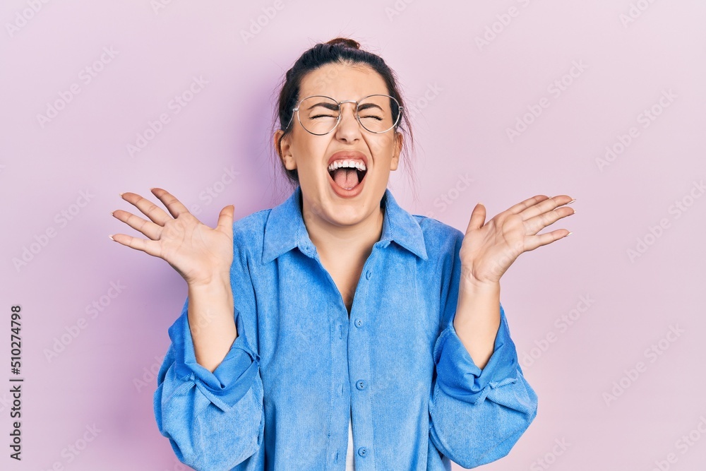 Canvas Prints Young hispanic woman wearing casual clothes and glasses celebrating mad and crazy for success with arms raised and closed eyes screaming excited. winner concept