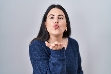 Fototapeta premium Young brunette woman standing over isolated background looking at the camera blowing a kiss with hand on air being lovely and sexy. love expression.