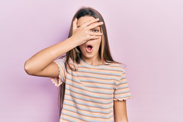 Young brunette girl wearing casual striped t shirt peeking in shock covering face and eyes with hand, looking through fingers afraid