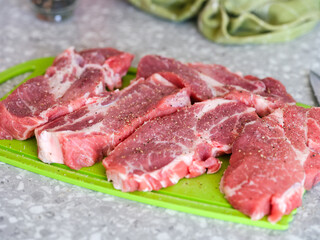 Peppered and salted raw pork slices on a green cutting board