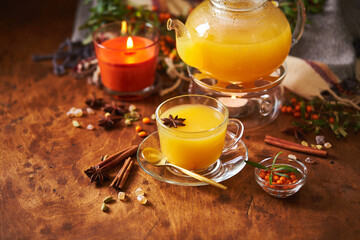 Glass teapot and sea buckthorn tea cup with cinnamon sticks and star anise on wooden background
