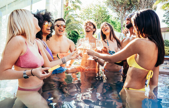 Multiracial friends drinking champagne together on pool party - Diverse young people having fun at a holiday resort - Summer vacations concept with guys and girls hanging outside together