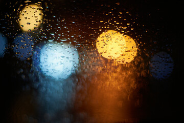 Światła drogowe za szybą w deszczu. Duże krążki kolorowych świateł, na szybie krople deszczu. Jazda samochodem.