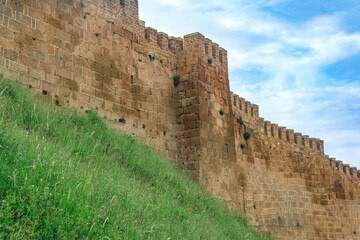 wall of a medieval fortress above a rampart overgrown with grass against the sky, Naryn-Kala citadel in Derbent