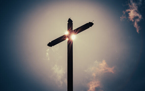 Wooden cross with sun and sky in background
