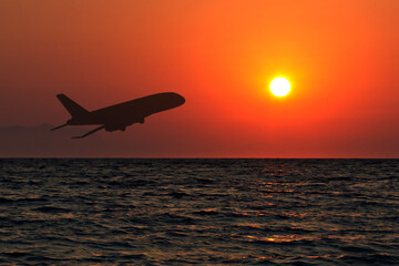 Fototapeta na wymiar travel agency, international flights, hotel and air tickets booking, silhouette of an airplane taking off at sunset on sky background over the sea