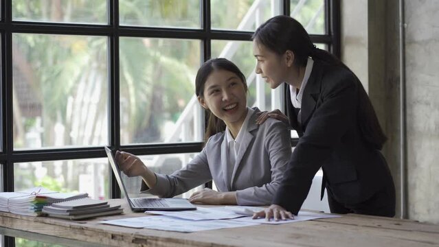 Two young business women in Asia brainstorm with colleagues on a new document project. that work together to plan strategies for success Enjoy working as a team in a small office.