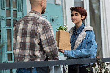 Smiling large handsome florist and owner of floral store he giving to the customer woman some plants on the eco bag he discussing a bit