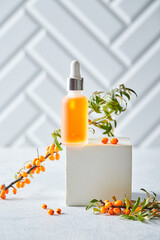 Glass bottle with sea buckthorn oil, berries and branches of sea buckthorn on light background