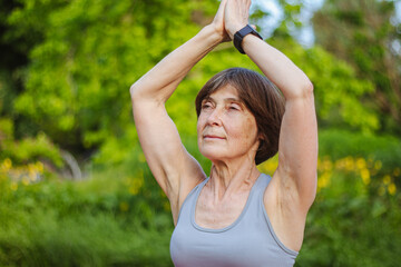 Naklejka na ściany i meble An old slender woman does yoga in the park
