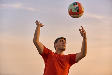 young man playing volleyball at the beach on a summer-day sunset