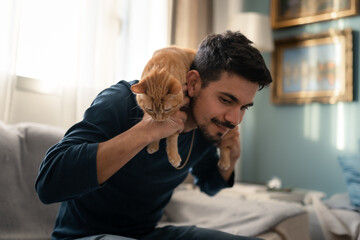 young man plays with a brown tabby cat in the living room