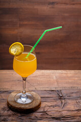 Fruit cocktail with a straw garnished with a slice of lemon in a large glass on a wooden table.