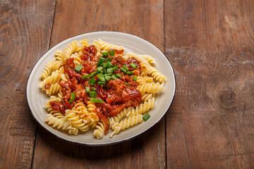 Beige plate with bolognese pasta on a wooden table sprinkled with green onions.