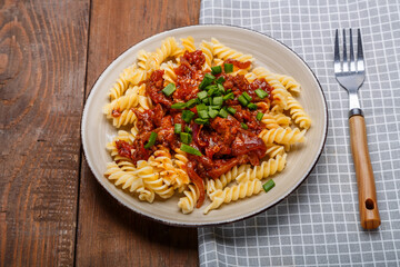 A plate with bolognese pasta on a wooden table next to a light napkin and a fork.