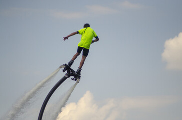 aquatic aviation, flyboarding, man in the green shirt flies on flyboard in the blue sky