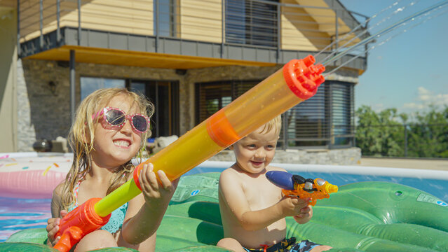 CLOSE UP: Happy brother and sister having fun at water fight in the garden pool