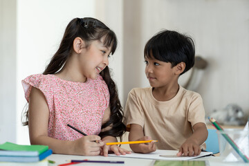 Asian children boy and girl using pencil writing something in book at classroom. Asian son and duaghter doing homework while sitting at desk at home. Kid learning by drawing. Education concept