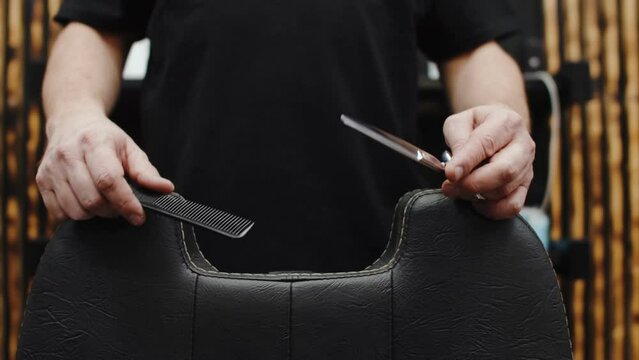 Haircut master puts his hands with scissors for milling and a hair clipper on the barber chair, concept of readiness for work. Barber's hands hold a working tool over the chair, close-up