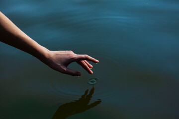 a woman's hand gently touches the water in the pond, a close horizontal photo on the theme of...