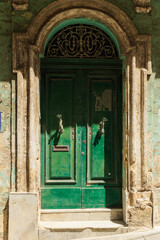 Fototapeta na wymiar dilapidated shabby green door on an old building. Fish-shaped door handles