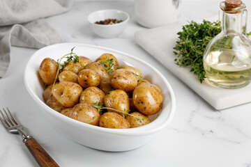 Young roasted baby potato in a white baked dish on mabrle background.