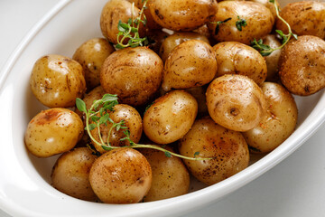 Roasted  baby new young potatoes in white baked dish with thyme, close up.