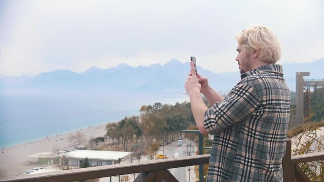 Young blonde man takes photos of the sea view