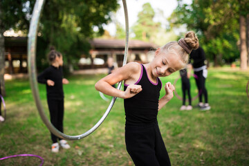 Girl doing exercise with hoop on rhythmic gymnastics training with other trainees outdoors in sports camp in summer