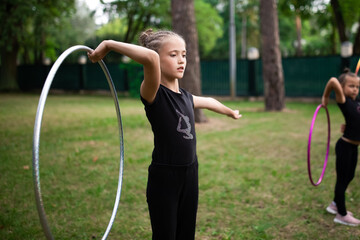 Girl doing exercise with hoop on rhythmic gymnastics training with other trainees outdoors in sports camp in summer © Olena Shvets