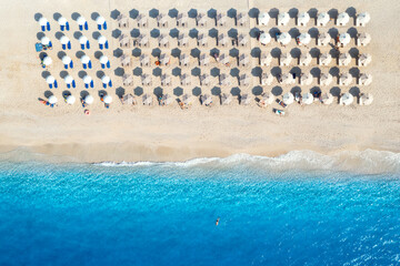 Aerial view of blue sea, sandy beach with sun beds and umbrellas at sunset in summer. Tropical...