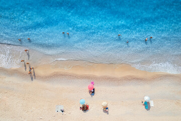Fototapeta na wymiar Aerial view of adriatic sea, waves, sandy beach and umbrellas with lying people at sunset in summer. Tropical landscape with clear turquoise water. Top view from drone. Lefkada island, Greece. Travel