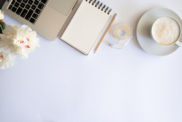 Stylish workspace with cup coffee, paper, laptop and pink peony flowers. Woman working table. Top view, flat lay, copy space.Pink peonies bouquet. Top view feminine background.Spring summer background