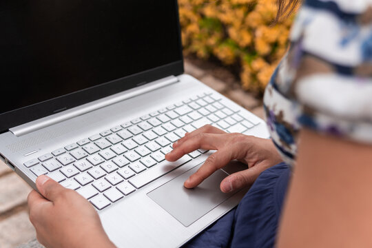 Woman scrolling on the touchpad of her laptop outdoors. Close-up image of the hands of a young girl moving the digital mouse of her computer to do university homework. Concept of technology life.