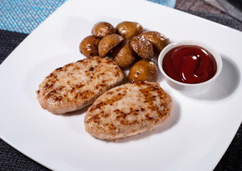 Two chicken cutlets with potatoes and tomato ketchup on white plate