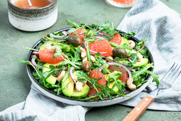 Healthy vegan salad with arugula, avocado, juicy grapefruit, cashews and dressing with olive oil, honey and wine vinegar. Green rustic kitchen table, top view, copy space