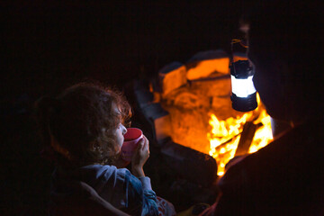 Dad and daughter sit at night by the fire in the open air in the summer in nature. Family camping...