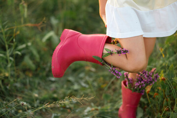 Red rubber boots on the feet of a girl with a bouquet of wild flowers. Flowers in a boot, summer...