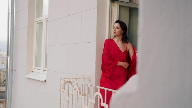 woman in a red silk robe goes out on a balcony in Moscow on a high floor