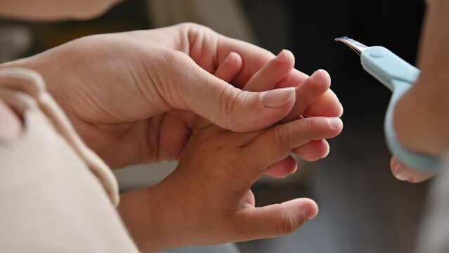 Mom cuts her child's nails with scissors. Child care, health and hygiene concept. Woman's hands with scissors and child's hands close-up. Toddler manicure, Home baby care