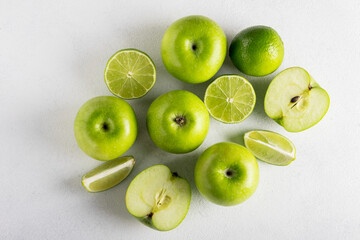 Top view of a composition of fresh ripe green apples and juicy limes on a light background. Selective focus.