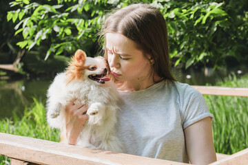 Young woman holds a Pomeranian puppy in her arms and is angry with him. The dog smiles and sticks out its tongue. The owner of the dog scolds her for disobedience.