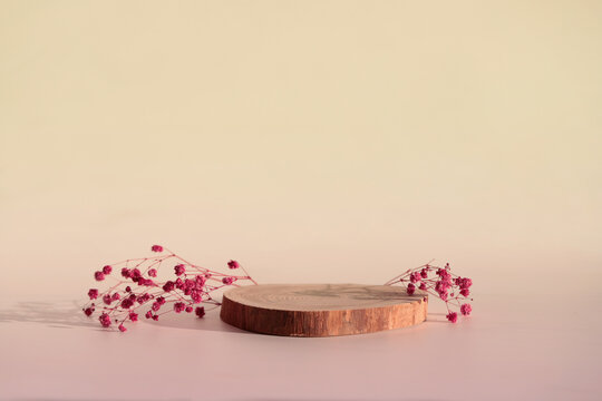 A round wooden felled cylindrical tree on a beige background with small red flowers of a minimalistic and geometric podium. High quality photo.