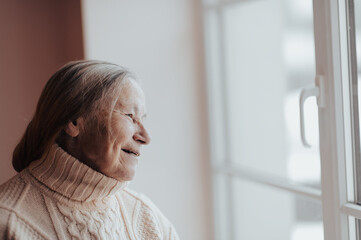 Obraz premium side view and smiling grandmother looking out the window