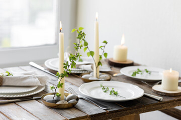Rustic zero waste wedding decor with natural elements. Wooden table, candles, linen napkins, branches with green leaves. Eco-friendly decoration for the special dinner. Romantic and cozy place