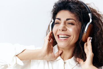 Portrait Of Enjoyed Happy Curly Beautiful Latin Woman Listening Cool Song In Headphones Smiling Looks Aside Isolated At White Studio Wall Background. Music Devices DJ Technology Huge Sale Concept