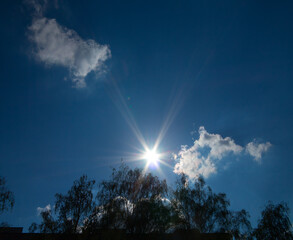 Slight summer cloudy in the summer sky. Afternoon sunbeams in the backlight over the trees and the roof of the house.